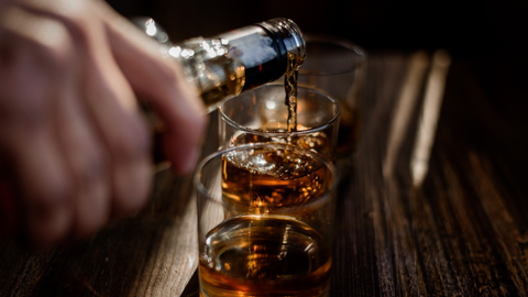 Pouring strong whiskey into glasses set on a wooden table