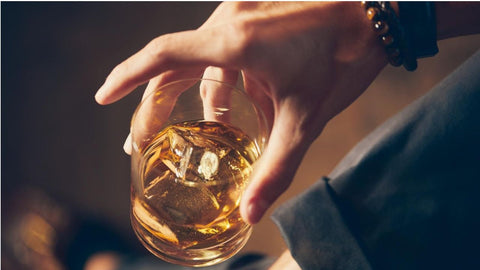 High-angle close-up of a man holding a glass of whiskey, showcasing rich amber color.