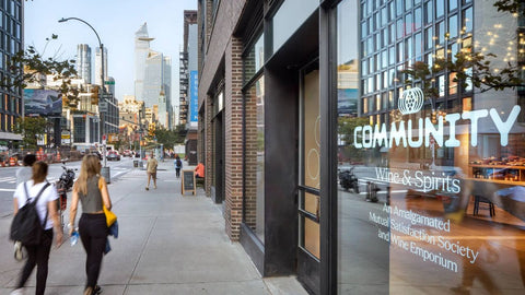 Street-level view of Community Wine & Spirits storefront with glass windows reflecting a modern city skyline