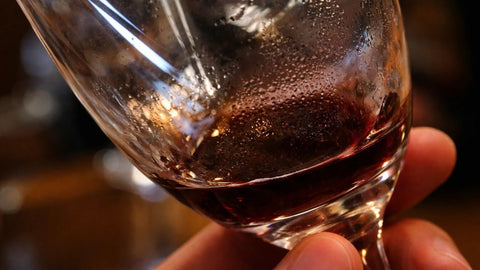 Close-up of a red wine glass tilted in hand, showing visible sediment